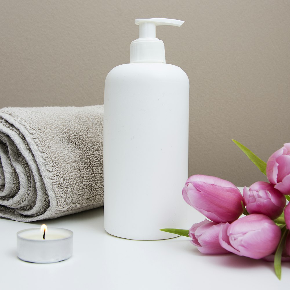 A warm spa still life with skincare products, a folded towel, and fresh flowers